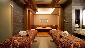 A hotel room with two beds, a large window, a wooden ceiling, and a bathroom with a mirror and sink.