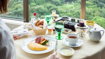 Uma mesa de café da manhã com diversos alimentos e bebidas, com um cenário de vegetação exuberante e um pagode.