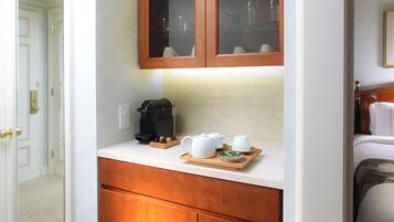 Habitación de hotel con un armario de madera, cafetera, teteras, tazas y una bandeja con un plato decorativo.