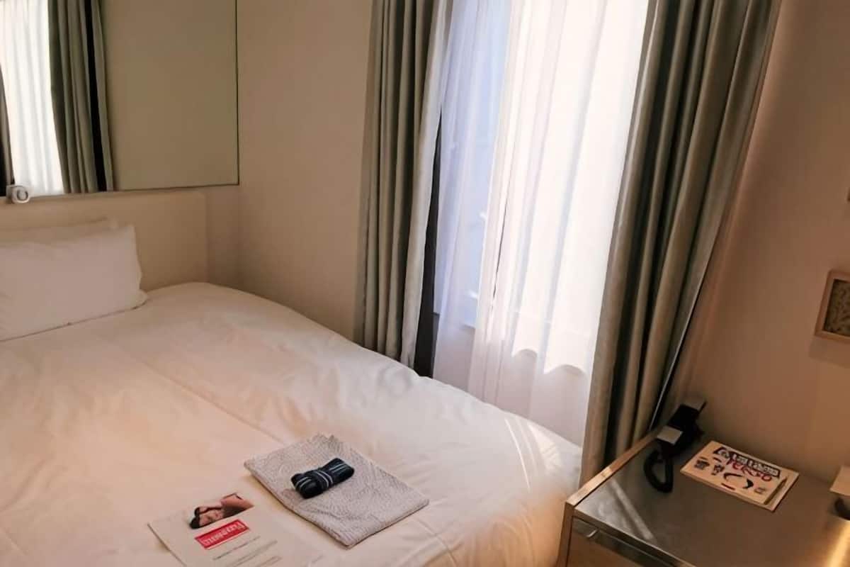 A hotel room with a bed, curtains, a bedside table, and a window.