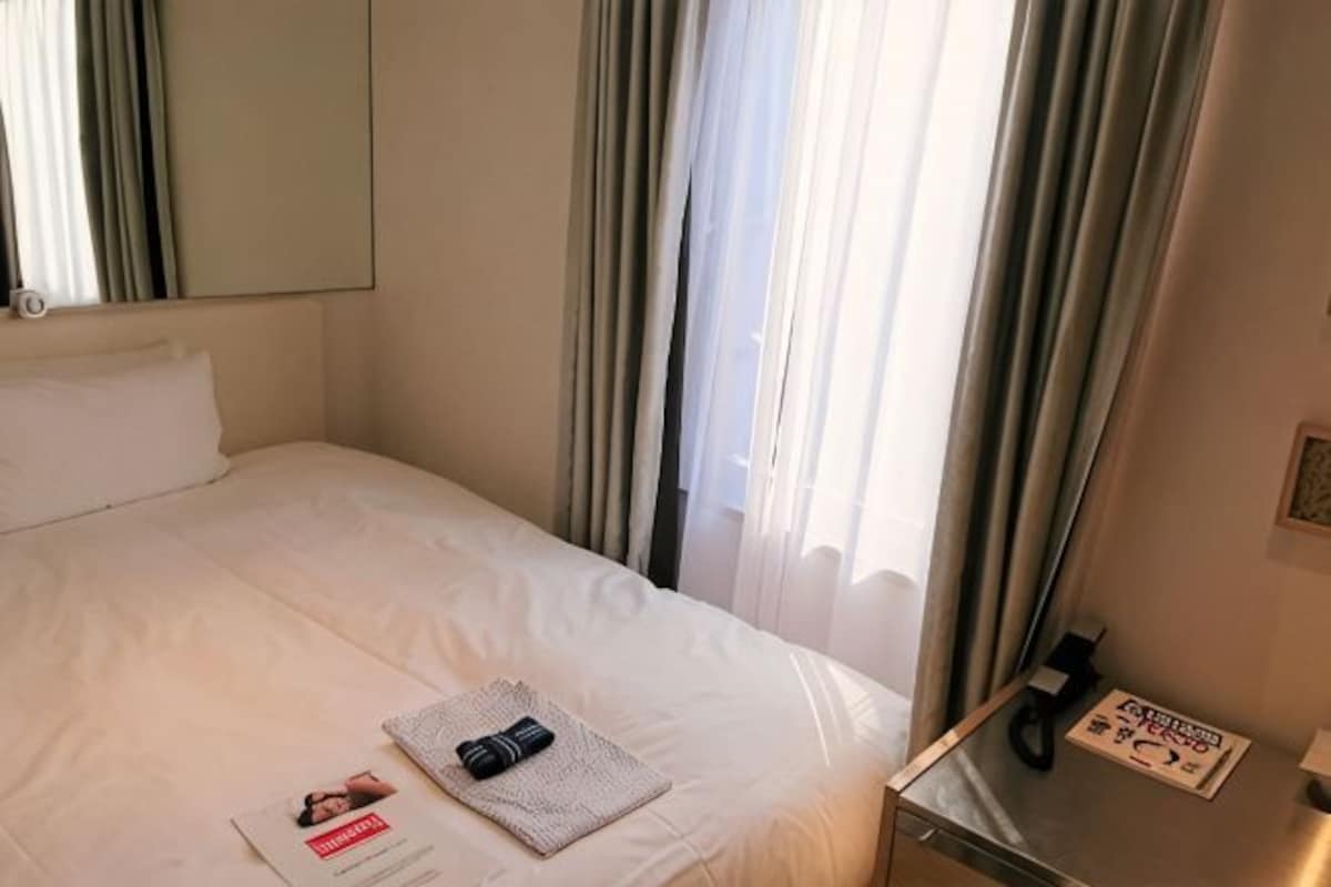 A hotel room with a bed, curtains, a bedside table, and a window.