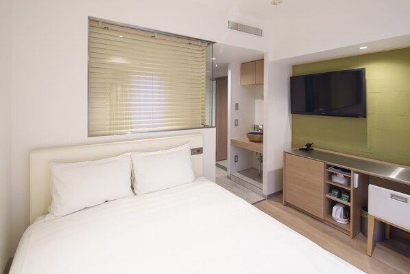 Quarto de hotel moderno com uma cama grande, televisão na parede, uma secretária pequena e um closet espaçoso.