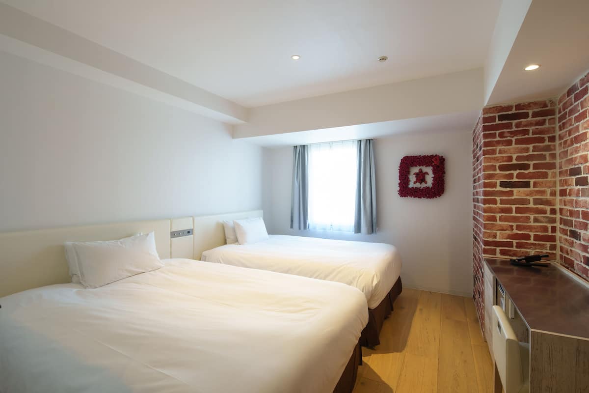 A hotel room with two beds, a brick wall, and a window with curtains.