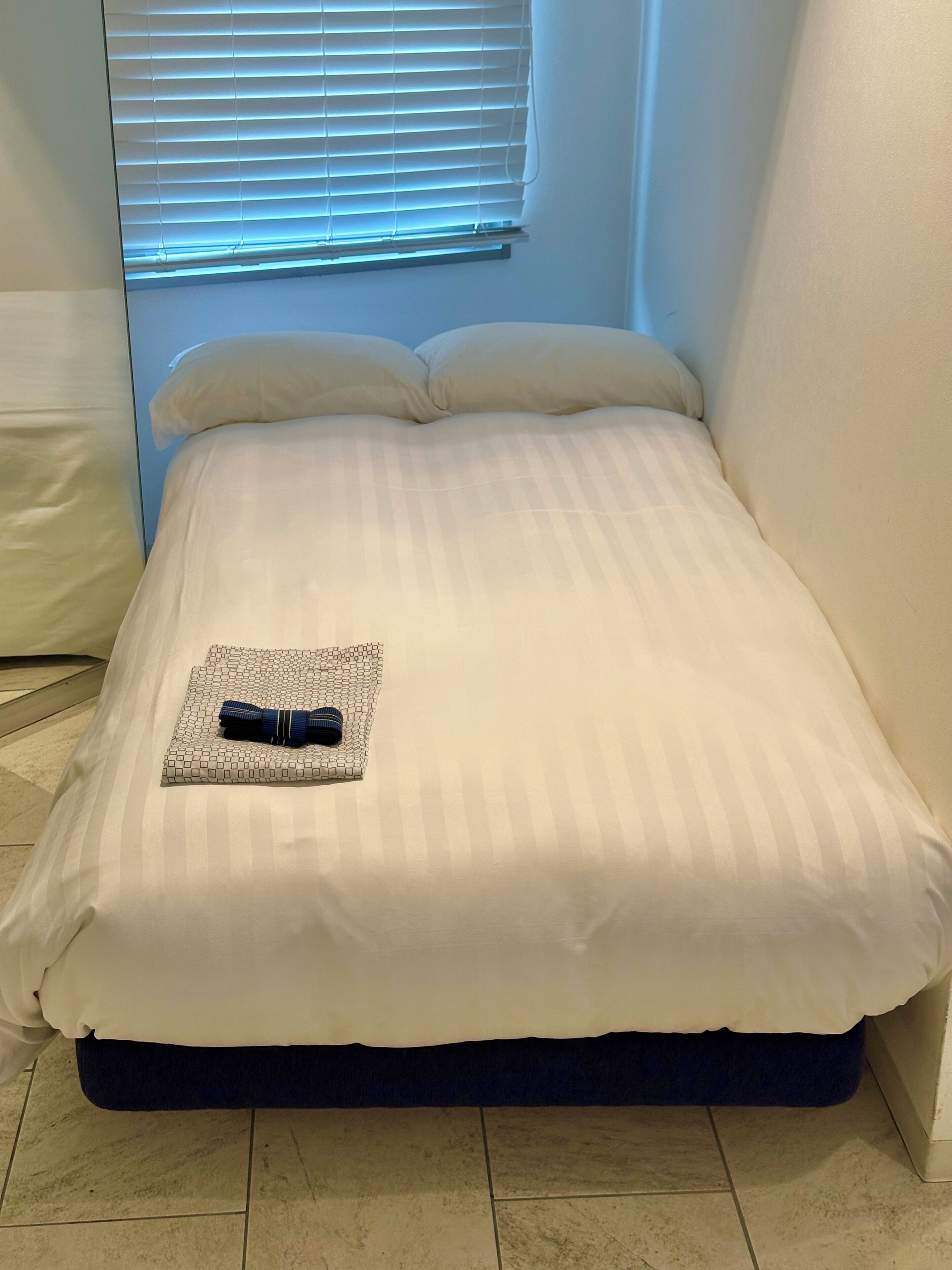 Una cama bien tendida con una almohada y una toalla doblada encima.
