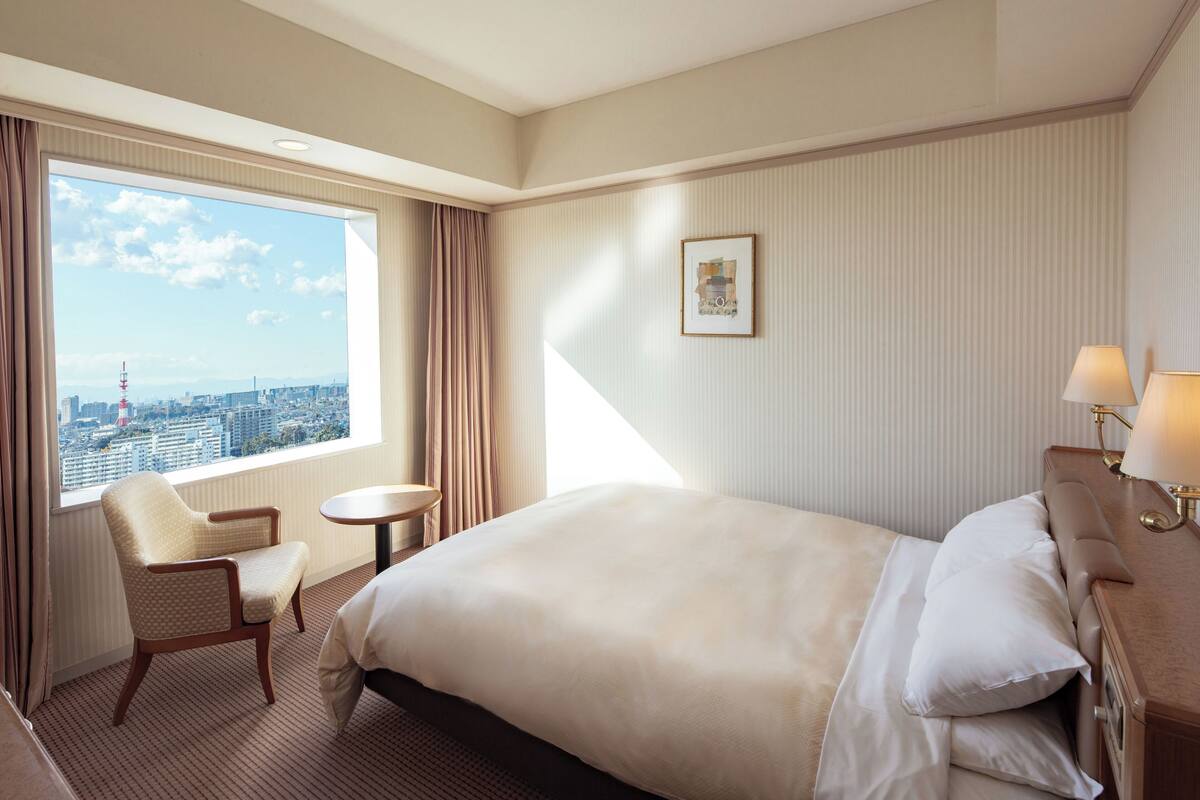 Een hotelkamer met een groot bed, een stoel, een tafeltje en een raam met uitzicht op de stad.