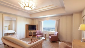 Habitación de hotel con un ventanal grande, televisor de pantalla plana, sofá, sillón y una mesita.