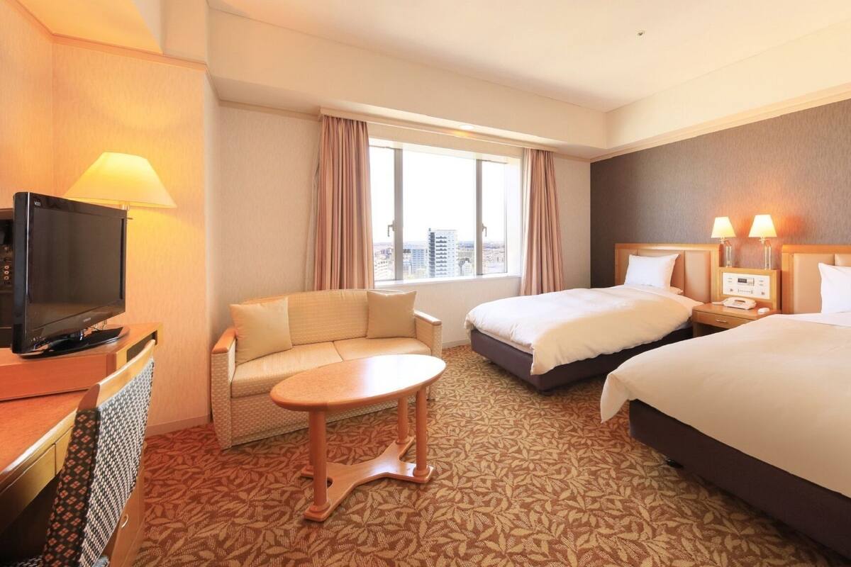 Een hotelkamer met een bank, twee bedden, een televisie en een klein tafeltje.