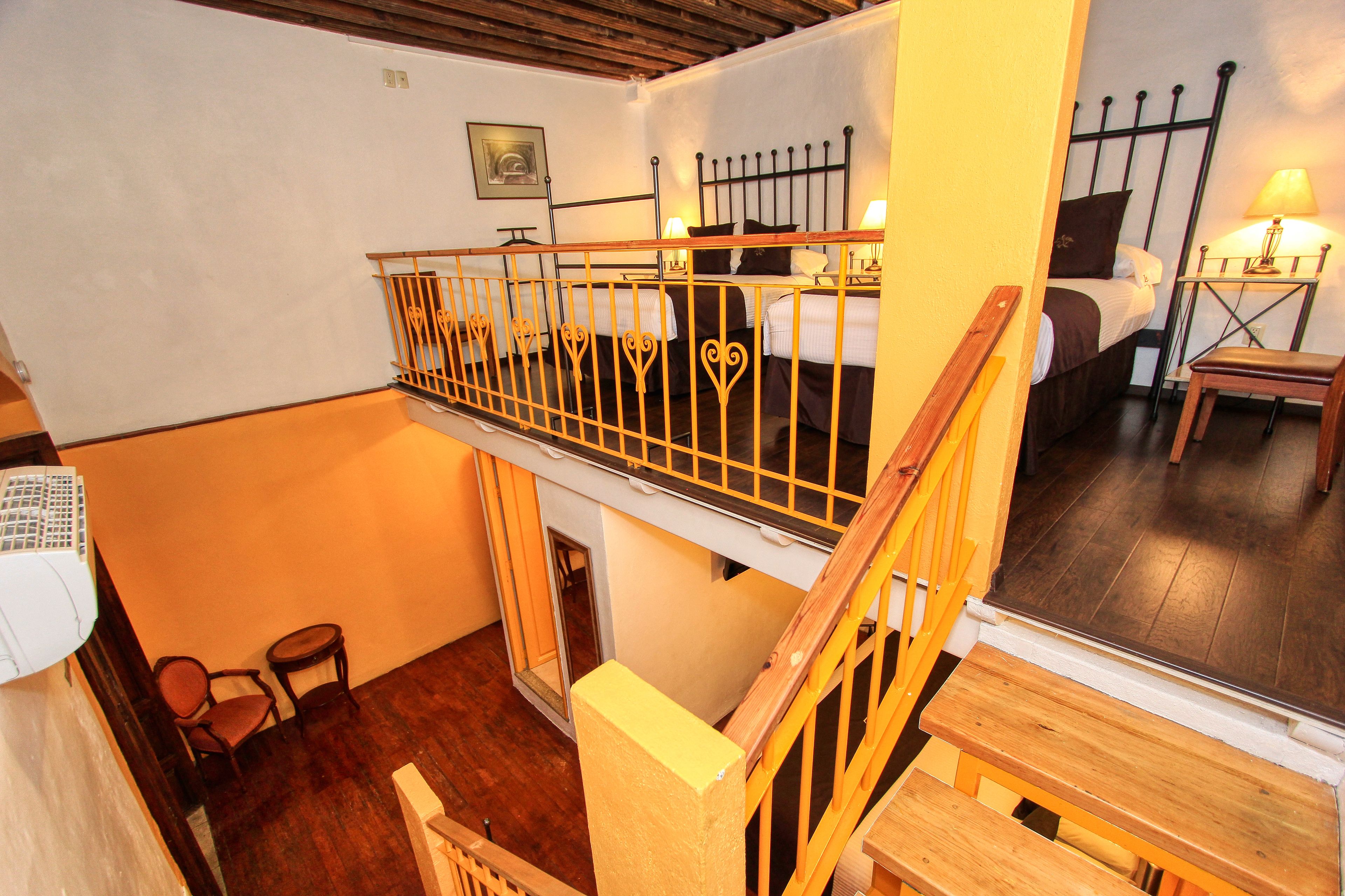 Una habitación con una cama, una silla, una mesita y una escalera.