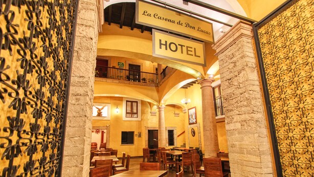 A hotel interior with multiple dining tables and chairs, a balcony, and a sign indicating the hotel's name.