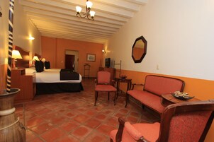 Habitación de hotel con cama, dos sillas, una mesita, un espejo y una lámpara.