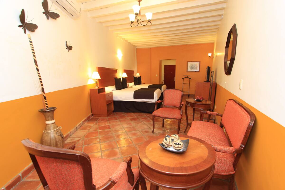 Habitación de hotel con cama, dos sillas, una mesita, lámpara y un florero.