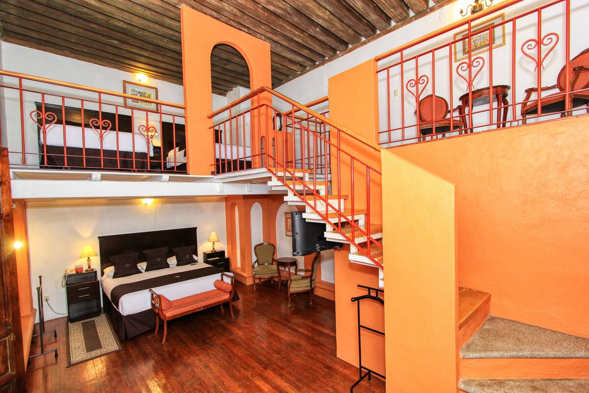 Una habitación de hotel con cama, mesita de noche, lámpara y un pequeño rincón de estar.