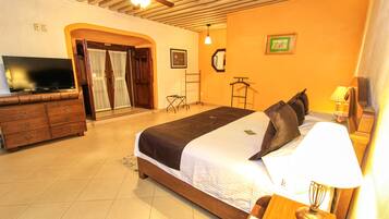 A hotel room with a bed, a TV, a wooden dresser, a lamp, and a door leading to a balcony.