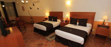 A hotel room with two beds, a desk, chairs, and a small table.