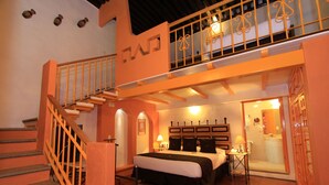 A hotel room with a bed, a desk, a chair, a small table, a mirror, a window, and a staircase.