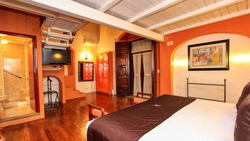 Habitación de hotel con cama, televisor, puerta de madera y un cuadro en la pared.