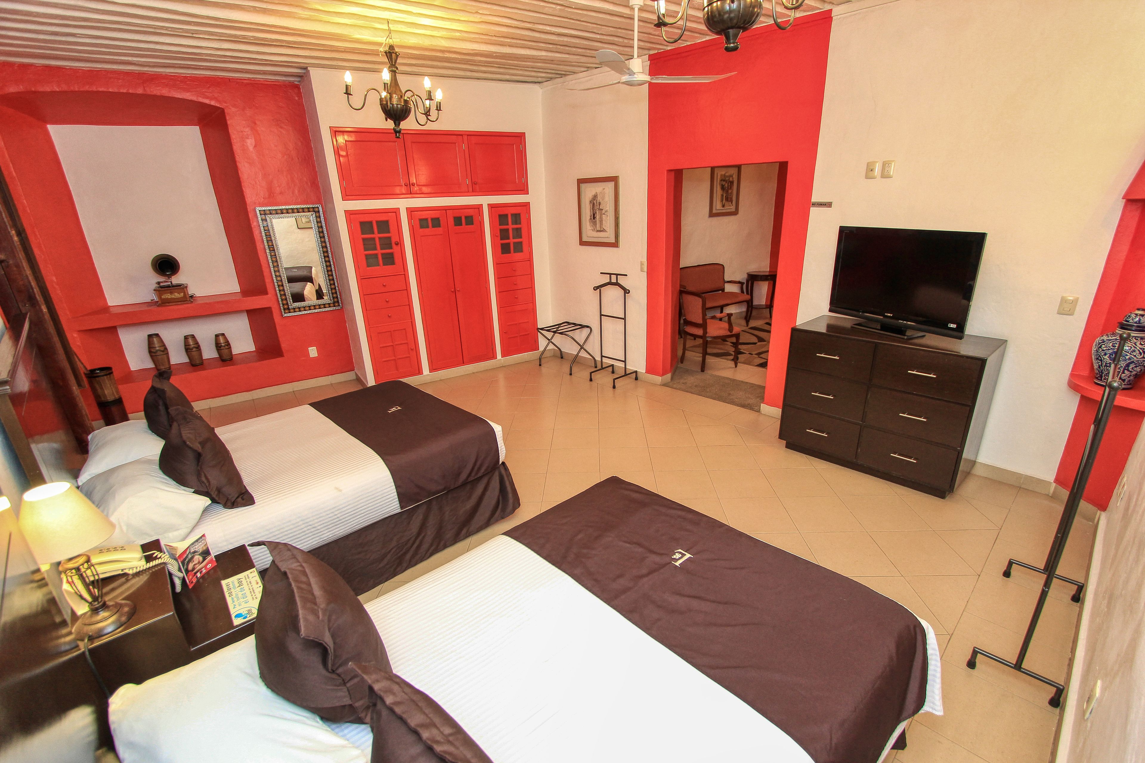 Een hotelkamer met twee bedden, een televisie, een bureau met een lamp en een rode wand.
