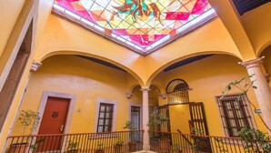 A yellow-walled interior with a stained glass window, arched balconies, and potted plants.