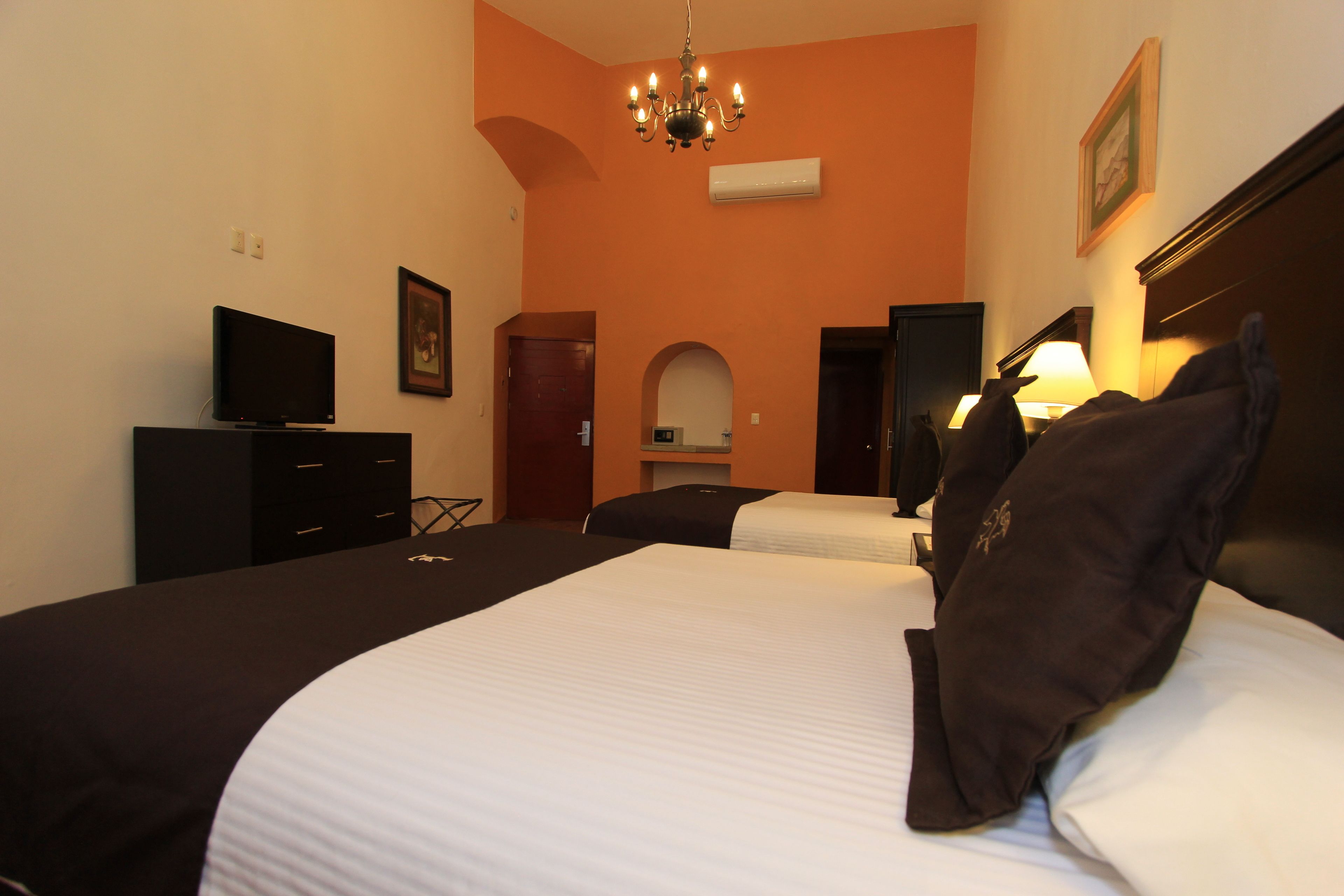 A hotel room with two beds, a TV, a chandelier, and a picture on the wall.