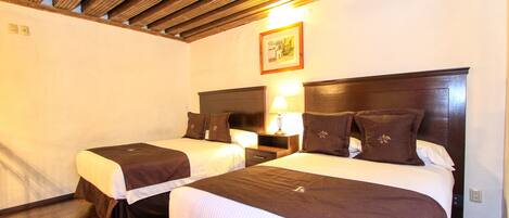 A hotel room with two beds, wooden ceiling beams, a nightstand with a lamp, and a framed picture on the wall.