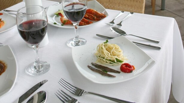 Uma área de refeições com mesas preparadas para uma refeição, incluindo pratos de comida e taças de vinho.