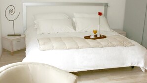 Quarto bem arrumado com uma cama grande, uma mesa de cabeceira, uma cadeira e uma pequena mesa com uma bandeja e um vaso.