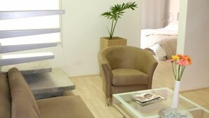 Uma sala de estar moderna com um sofá, uma mesa de centro de vidro, uma poltrona e um vaso com planta.