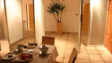 A dining area with a table set for two, a potted plant, and a brick wall.