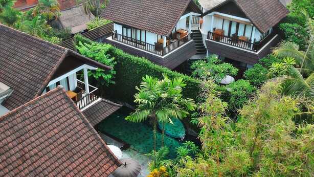 Um conjunto de casas de estilo tradicional com telhados de palha, cercado por vegetação exuberante e uma pequena piscina.