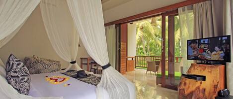 Une chambre à coucher avec un lit à baldaquin, une télévision et une vue sur un jardin tropical.