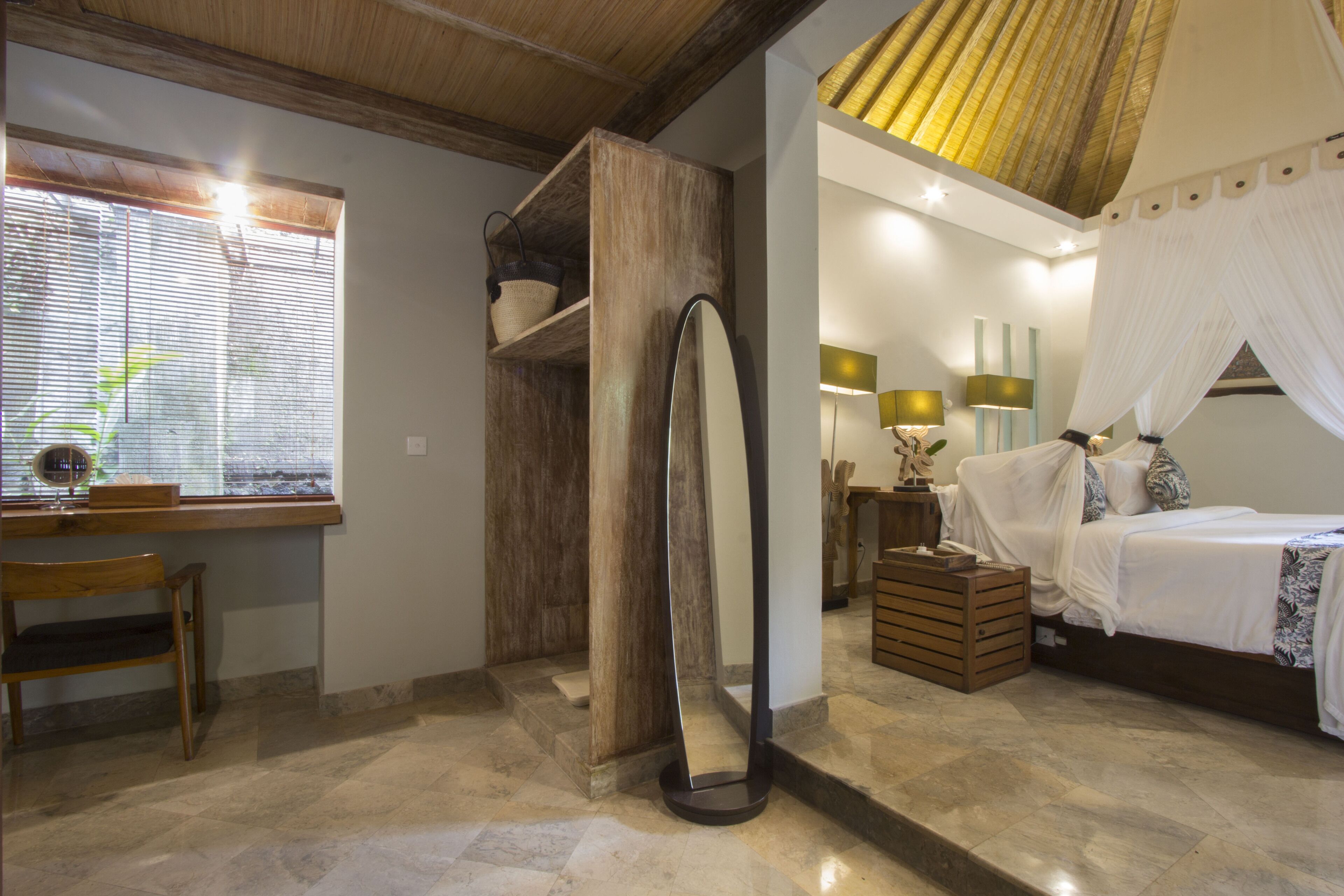 Una habitación con cama, escritorio, espejo y ventana con persianas.