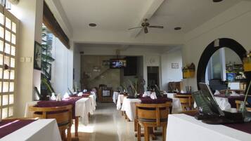 Ein Restaurant mit Holztischen und -stühlen, weißen Tischdecken und einem Deckenventilator.