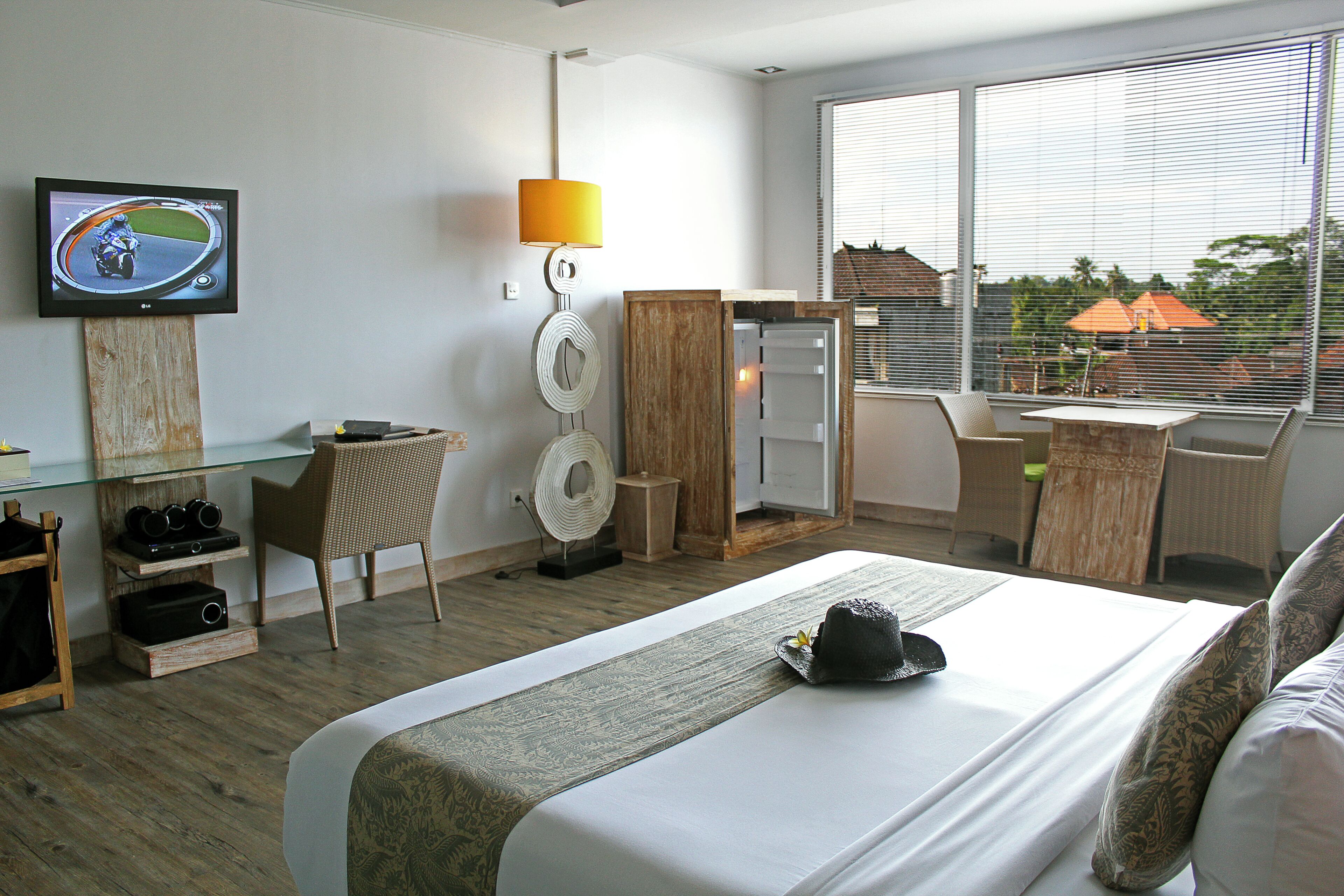 Habitación de hotel con cama, escritorio, silla, televisión y ventana con vista a casas.