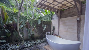 A modern bathroom with a freestanding bathtub, surrounded by lush tropical plants and a wooden pergola.