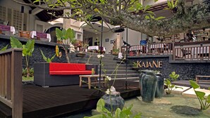 Um jardim interno tranquilo com um deck de madeira, um sofá vermelho e um elemento decorativo com água chamado "KAJANE".