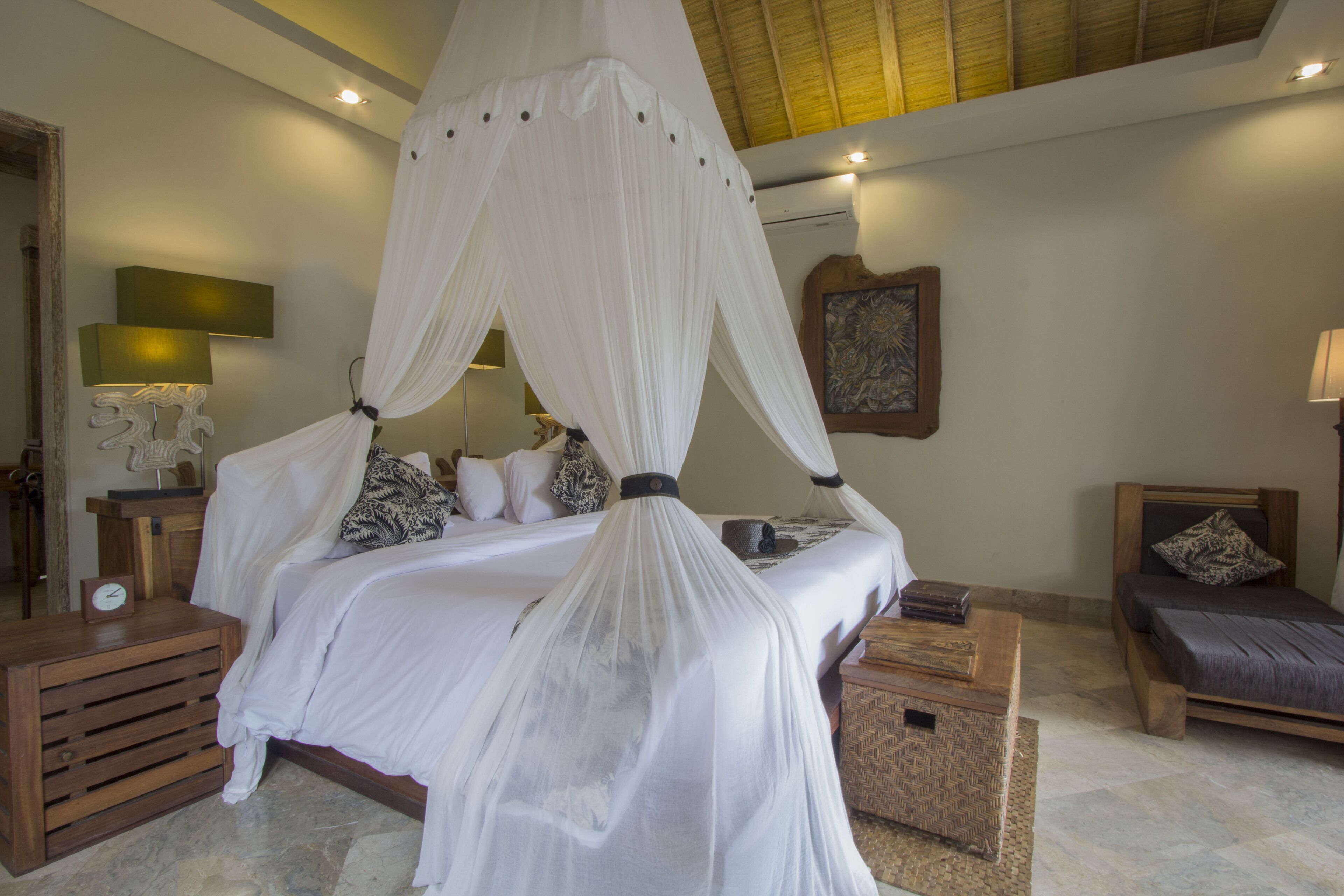 A bedroom with a four-poster bed, a bedside table, a nightstand, a wooden bench, and a small bedside table with a lamp.