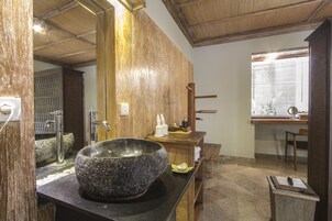 A bathroom with a large stone basin, wooden accents, and a window with blinds.