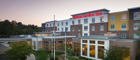 Un Hilton Garden Inn de varios pisos con un diseño moderno, que combina fachadas de ladrillo y vidrio, y un césped y jardín bien cuidados.