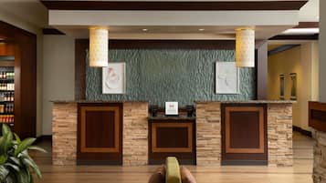 Ein Hotel-Empfangsbereich mit einer Steintheke, zwei gerahmten Kunstwerken und einem Empfangstresen.