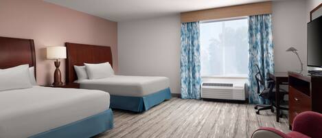 A hotel room with two beds, a desk, a chair, a TV, and a window with curtains.