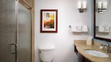 A bathroom with a toilet, sink, and shower. There is a framed picture on the wall and two wall-mounted light fixtures.