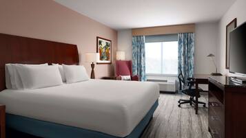 A hotel room with a large bed, a desk with a chair, a TV, and a window with curtains.