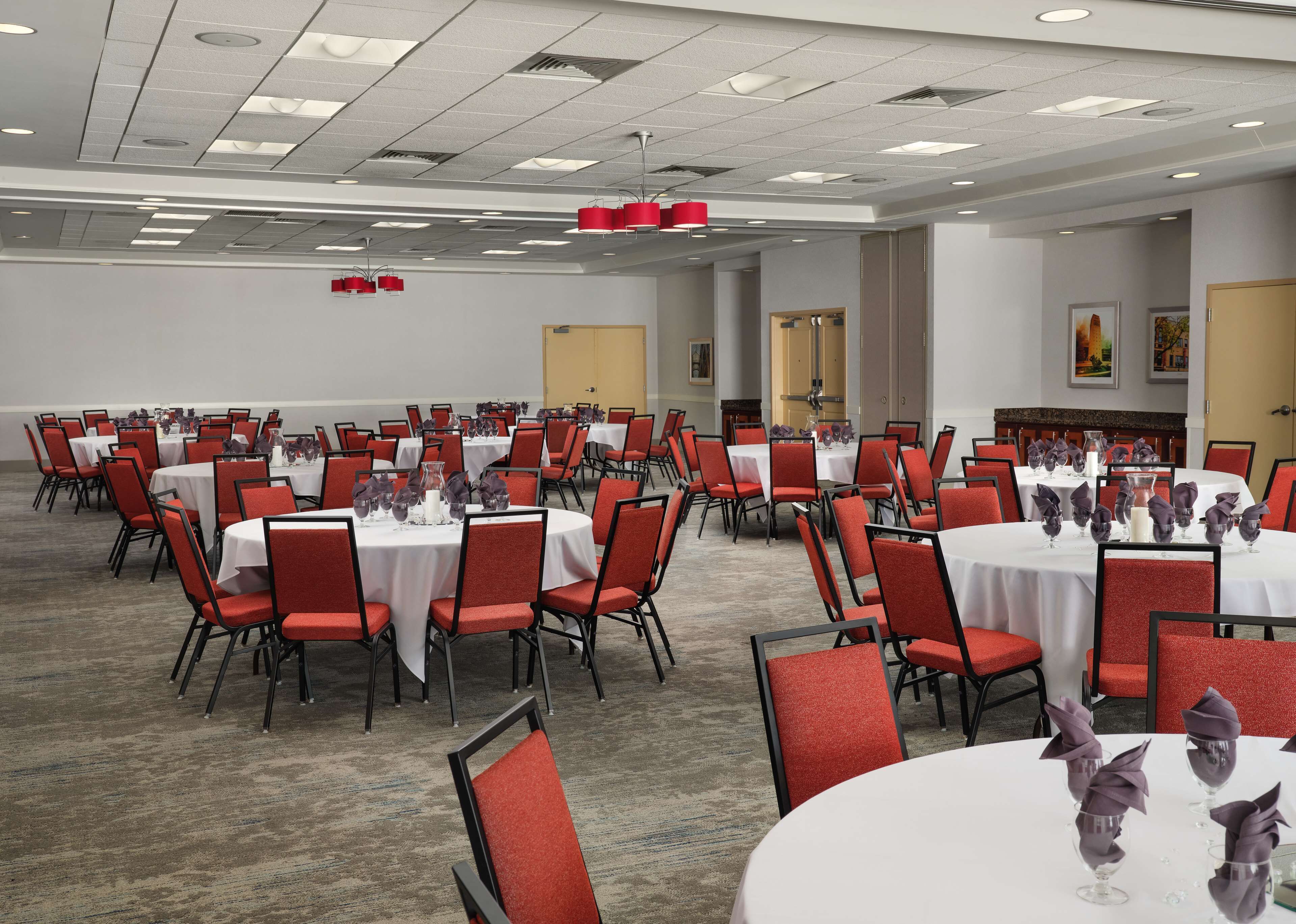 A conference room with multiple round tables, red chairs, and white tablecloths.
