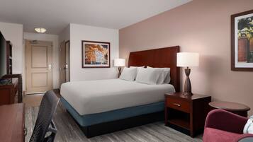 A hotel room with a large bed, two bedside tables with lamps, a desk, a chair, and a framed picture on the wall.