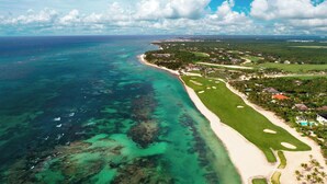 Vue aérienne d’une zone côtière comprenant un terrain de golf, une plage et des immeubles résidentiels.