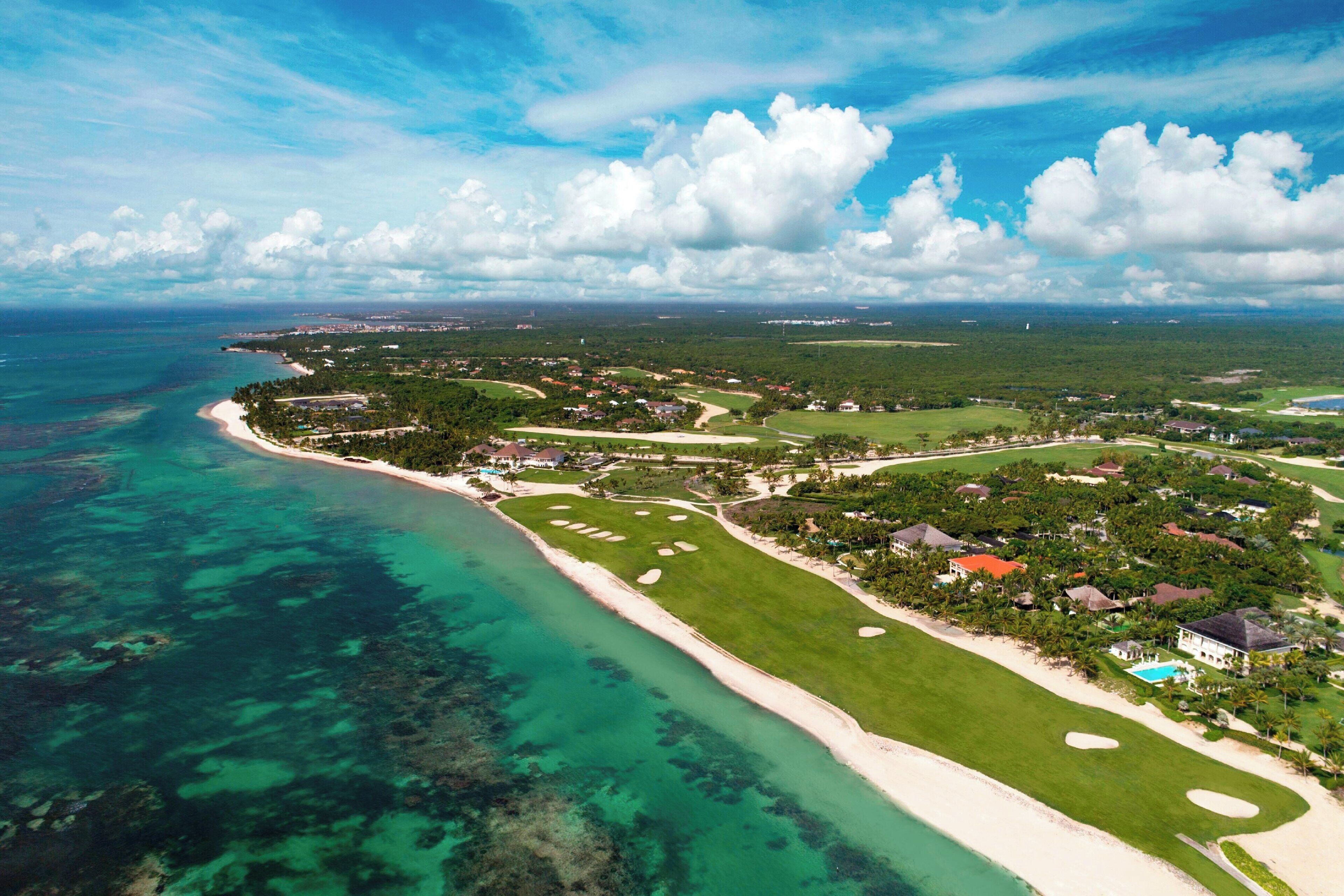 Vue aérienne d’une station balnéaire avec une plage de sable, des eaux turquoise et limpides, et une végétation luxuriante.
