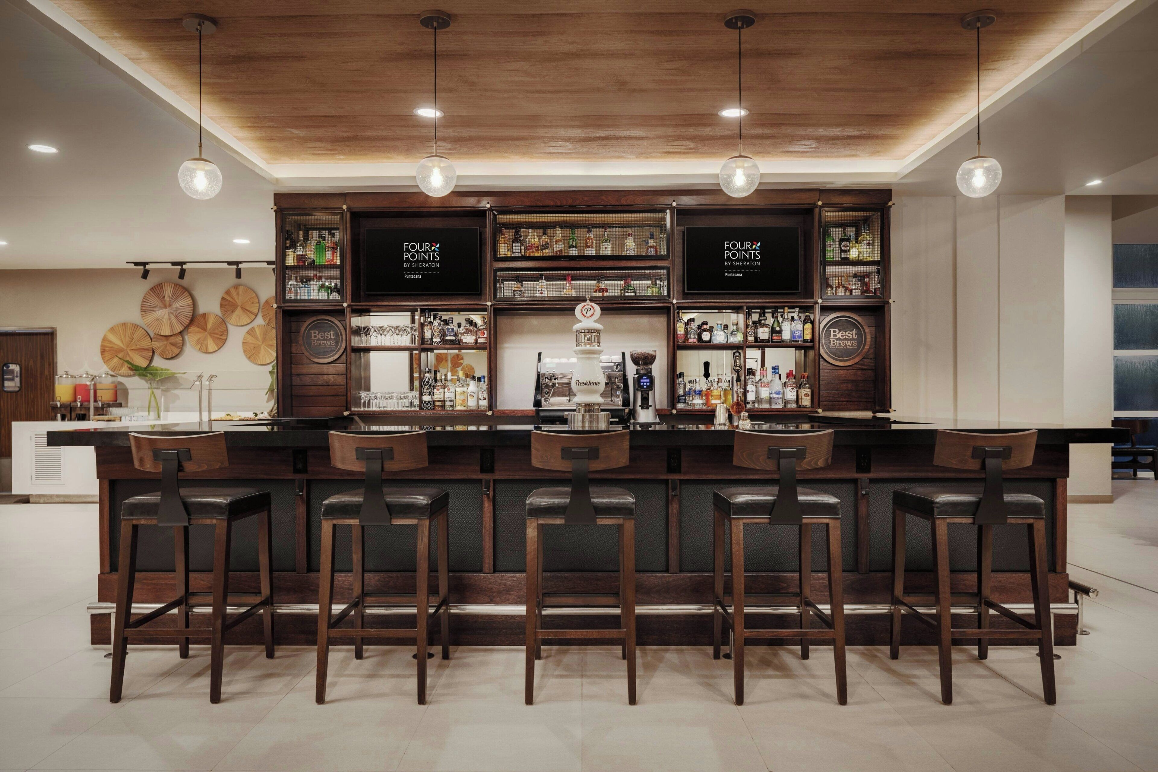 Un espace bar avec des tabourets de bar en bois, des étagères remplies de bouteilles et des lampes suspendues.