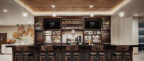 A bar area with wooden bar stools, shelves stocked with bottles, and hanging pendant lights.