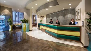 Un espace d’accueil moderne, doté d’un comptoir d’accueil incurvé, de deux réceptionnistes et d’un coin salon avec des canapés et des plantes en pot.