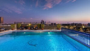 Une piscine sur le toit offrant une vue panoramique sur la ville, des chaises longues et des plantes en pot.
